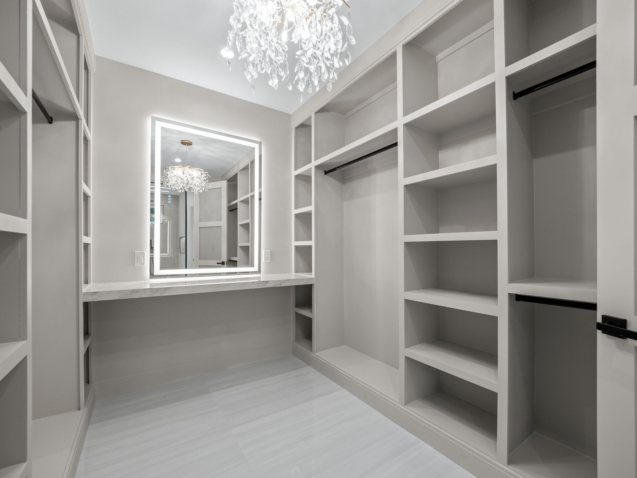 Custom walk-in closet with crystal chandelier and lit vanity